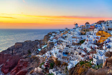Greece vacation background. Famous iconic Oia village with traditional white houses and windmills during colorful sunset. Santorini island, Greeceの写真素材