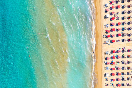 Top view aerial drone photo of Banana beach with beautiful turquoise water, sea waves and red umbrellas. Vacation travel background. Ionian sea, Zakynthos Island, Greece.の写真素材