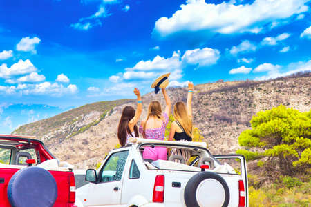 Travel by car, vacation concept. Three girls in a offroad car with open top against blue cloudy sky.の写真素材