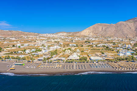 Top view aerial drone photo of black Perissa beach with beautiful turquoise water, sea waves and straw umbrellas. Vacation travel background. Aegean sea, Santorini Island, Greece.のeditorial素材