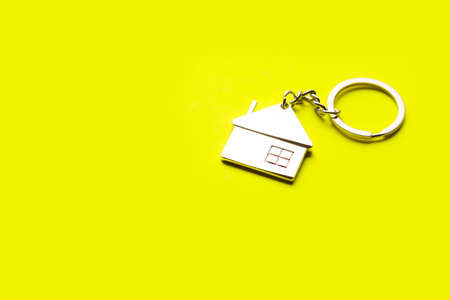 Metallic house shaped keychain on yellow background.の写真素材
