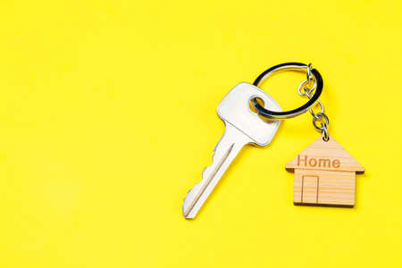 Wooden house shaped keychain and key on yellow background. free space.の写真素材