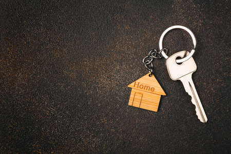 Wooden house shaped keychain and key on stone background. free space.