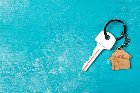 Wooden house shaped keychain and key on blue wooden background. free space.の写真素材