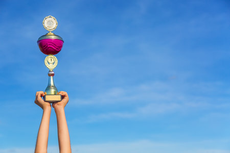 Childs hands holding winner trophy cup against blue sky background. Victory concept. Free space for your text.の写真素材