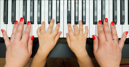 Piano musical keyboard with hands of little daughter and mother playing music. Top view. Family conceptの写真素材
