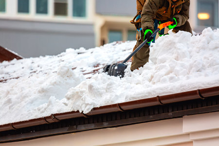 Communal services worker industrial climber removes snow from the building roof in winter. Cleaning city streets, roads and buillding roofs after snow storm in Moscow, Russiaの写真素材