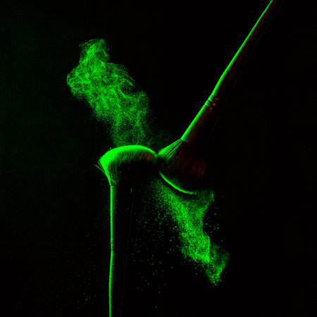 Make up cosmetic brushes with powder blush explosion on black background. Skin care or fashion concept. Green neon lighting.の写真素材