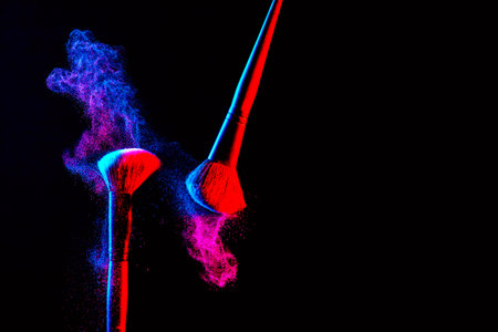 Make up cosmetic brushes with powder blush explosion on black background. Skin care or fashion concept. Nice red and blue neon lighting. Free space.の写真素材