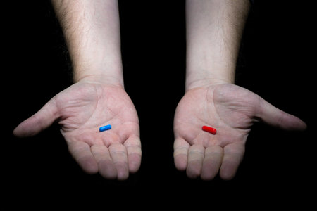 Hands holding red and blue pills capsules on black backgroundの写真素材