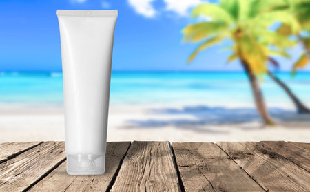 White blank cream tube Mockup template. White blank cream tube on wooden pier against blurred paradise beach with white sand and coconut palms. Care about hands, face, legs and body skin at a vacation. Empty place for text or logoの写真素材