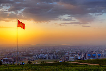 Bishkek city view with highest flagpole with the National flag of Kyrgyzstan on Mount Boz-Boltok during colorful sunset. Bishkek - capital city of Kyrgyzstan.の写真素材
