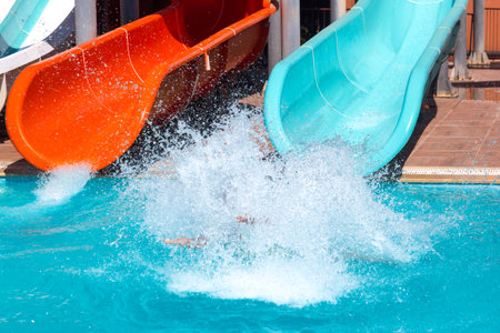 Young girl slided down a blue water slide with a lot of water splashes in a pool. Vacation conceptの写真素材