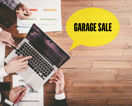 BUSINESS TEAM WORKING IN OFFICE WITH GARAGE SALE SPEECH BUBBLE ON DESKの写真素材