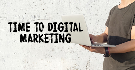 Young man using laptop and TIME TO DIGITAL MARKETING concept on wall backgroundの写真素材