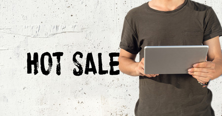 Young man using tablet pc and HOT SALE concept on wall backgroundの写真素材
