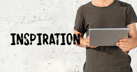 Young man using tablet pc and INSPIRATION concept on wall backgroundの写真素材