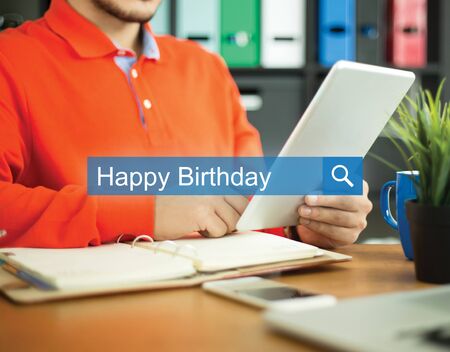 Young man working in an office with tablet pc and searching HAPPY BIRTHDAY word on internetの写真素材