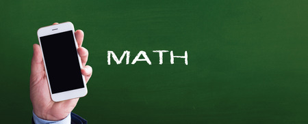Smart phone in hand front of blackboard and written MATHの写真素材
