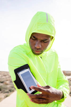 Vertical shot of young black runner with yellow jacket and bracelet who presses a button on his cell...