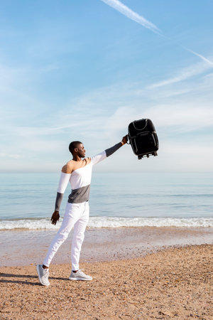 Portrait of a young black boy picking up a suitcase on the beach. Concept of travel.の写真素材