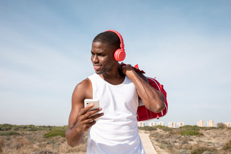 Portrait of young black athlete smiles while listening to music on his mobile with red headphones. Young man laughing while chatting.の写真素材