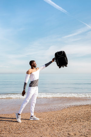 Portrait of a young black boy picking up a suitcase on the beach. Concept of travel.の写真素材