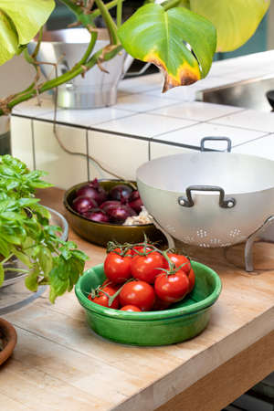 Tomatoes in a green bowl on a kitchen counter. Colander, basil and onions.
