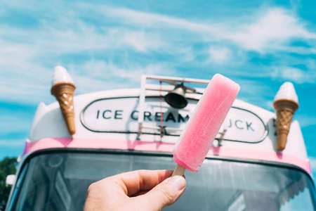 Pink ice cream with a pink ice cream truck or van in the background. Hand