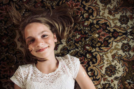 Smiling girl laying on the floor on a Persian carpet in a white dress.の写真素材