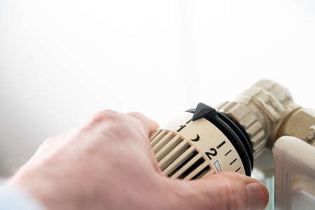 Close-up of hand turning thermostat down. Turn heating off. Gas price. Savings.の写真素材