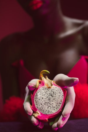 Black model holding sliced dragon fruit. Surreal fashion setting. Pink and blackの写真素材