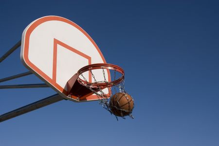 Basketball backboard against a clear blue sky with ball going through hoop