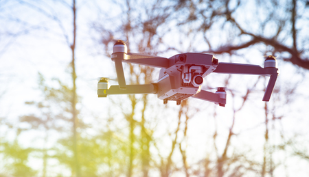 Drone flying in the blue sky, unmanned copter flight over blurred forest backgroundの写真素材