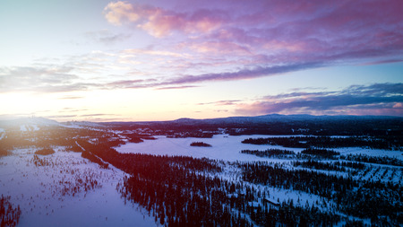 The Aerial view of snow-covered forest in time of sunny winter sunrise. Crowns of coniferous trees and clouds a bright are lighted up by rising sunの写真素材