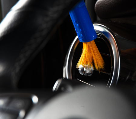 Brush cleaning off dust from the car interior details, control panel of the dashboard. A man cleaning car with cloth and brush. Car detailing.  Worker cleaning. Brush and cleaning solution to cleanの写真素材