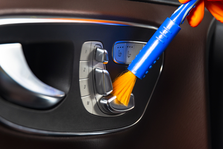Brush cleaning off dust from the car interior details, control panel of the windows.  A man cleaning car with cloth and brush. Car detailing.  Worker cleaning. Brush and cleaning solution to clean the interiorの写真素材