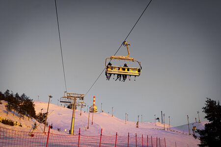 Silhouettes of skiers on chair lifts in the evening, sunsetの写真素材