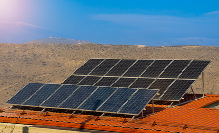 Photo  of solar panels, photovoltaics on the red roof of a house and a beautiful sky with mountains and sun. Alternative electricity source. Concept of sustainable resourcesの写真素材