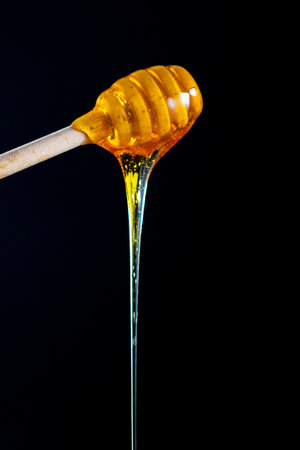 Honey dripping from dipper wooden honey stick over black backgroundの写真素材