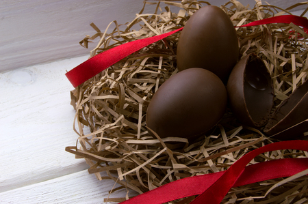 Chocolate eggs in nest with red ribbon on white wooden backgroundの写真素材