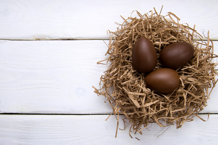 Chocolate easter eggs in nest on white wooden background top viewの写真素材