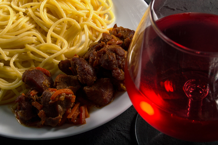 Pasta with beef meat in white plate and wine glasses on dark concrete backgroundの写真素材