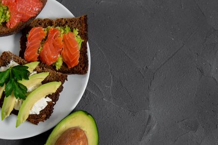 Two toast with avocado slice with cream cheese and smash avocado with red fish salmon and slice avocado with bone on white plate and concrete top viewの写真素材