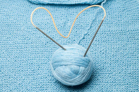 ball of blue wool with steel knitting needles