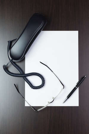 blank sheet of paper on the table with a pen, glasses and telephoneの写真素材