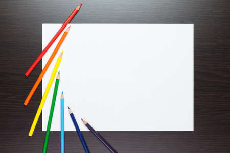 blank sheet of paper on the brown table with colorful pencilsの写真素材