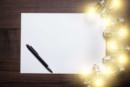 glowing bulbs and blank sheet of paper over wooden backgroundの写真素材