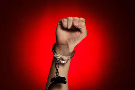 fist and handcuffs opened over red background conceptの写真素材