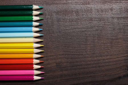 multicolored pencils on brown wooden table background
